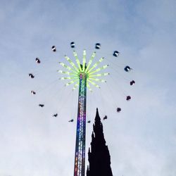 Low angle view of illuminated chain swing ride by silhouetted castle