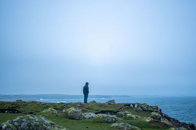 Man standing on rock by sea against sky