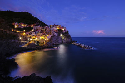 Scenic view of sea by illuminated buildings against sky at dusk