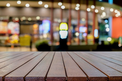 Empty wooden table against illuminated lights at restaurant