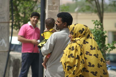 Rear view of friends standing against yellow wall