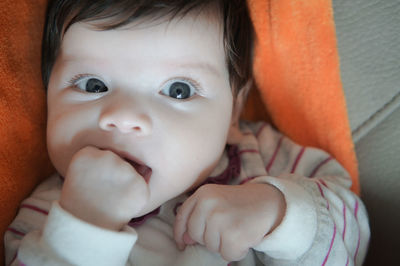 Close-up portrait of cute baby girl with fingers in mouth