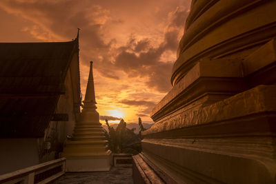 Low angle view of cross amidst buildings against sky during sunset