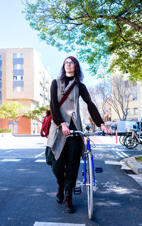 Young smiling woman walking on a city street with bicycle