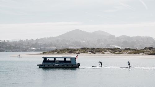 Silhouette people paddleboarding by boat sailing in river