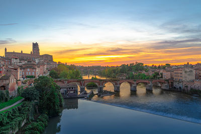 Arch bridge over river against sky during sunset