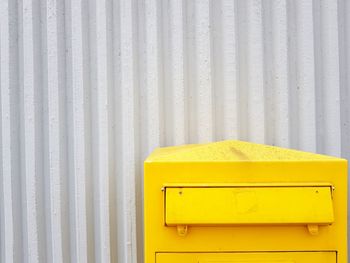 Yellow mailbox against corrugated iron