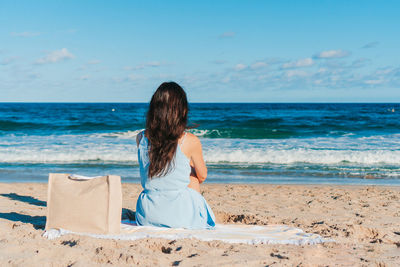 Rear view of woman sitting at beach against sky