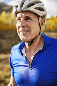 Smiling sweaty senior man wearing bicycle helmet while looking away on field