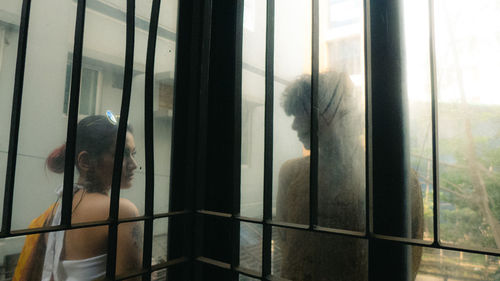 Silhouette of a girl and a boy standing, separated by a pillar behind a glass.