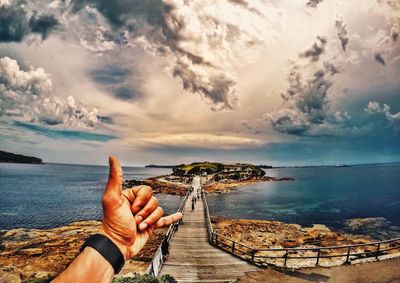 Cropped image of man gesturing shaka sign against footbridge on sea