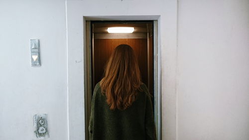 Rear view of woman standing against illuminated elevator