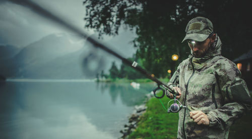 Man holding fishing rod standing by lake