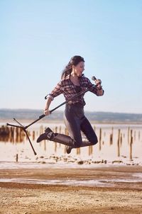 Beautiful singer jumping with microphone stand on field against sky