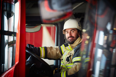 Portrait of confident male firefighter sitting in fire engine at fire station