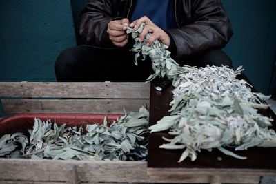 Midsection of vendor holding leaf vegetables at market stall