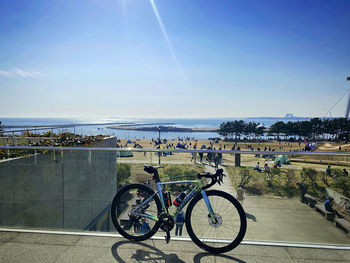 Bicycle parked by sea against sky on sunny day