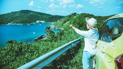 Side view of woman pointing towards sea while standing by car 