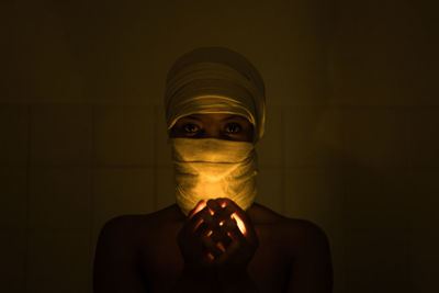 Close-up portrait of woman with covered face holding illuminated light in darkroom