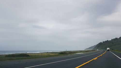 Empty road by sea against sky