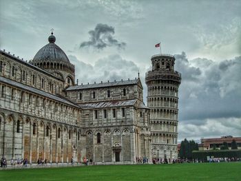 Leaning tower of pisa in a cloudy rainy day with people around and green grass