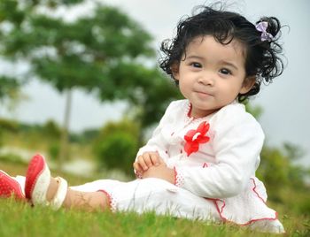 Portrait of cute baby girl sitting on grassy field against sky