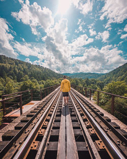 Rear view of man walking on railroad track against sky