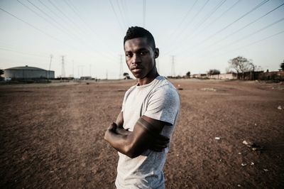 Portrait of young man standing on car against sky