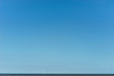 Scenic view of sea against clear blue sky and wind turbines in the lower ground