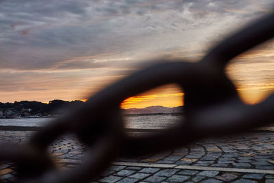 Scenic view of sea seen through fence during sunset