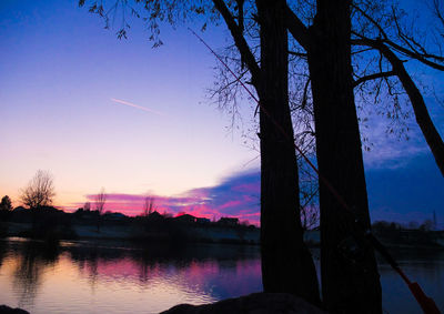 Silhouette trees by lake against sky during sunset