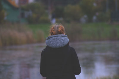 Rear view of woman standing against lake during winter