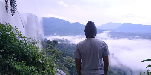 Rear view of man looking at mountains against sky