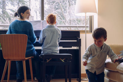 Mother and son playing piano by sibling at home