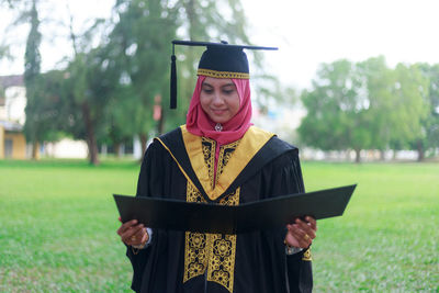 Woman in graduation gown standing on field