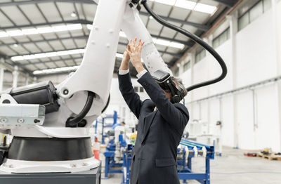 Businessman wearing virtual reality gesturing with arms raised in factory