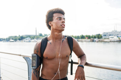 Thoughtful shirtless male athlete standing on promenade in city