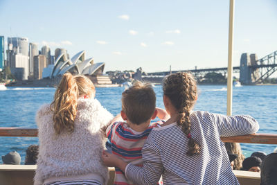 Rear view of people on sea by cityscape against sky