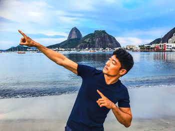 Mature man gesturing while standing at beach against sky