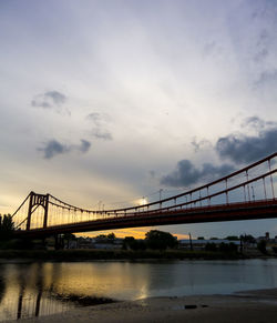Bridge over river in city against cloudy sky