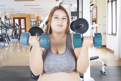 Portrait of smiling woman lifting dumbbells in gym