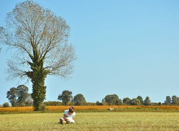 Girl sitting on grassy field against clear sky