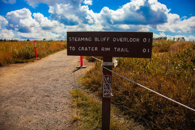 Information sign on road amidst field against sky