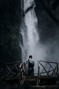 Man standing by railing against waterfall