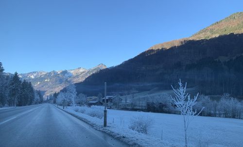 Road amidst snowcapped mountains against clear sky during winter