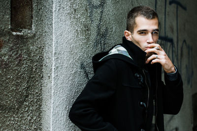 Young man smoking while standing against wall