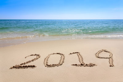 Text on sand at beach against sky