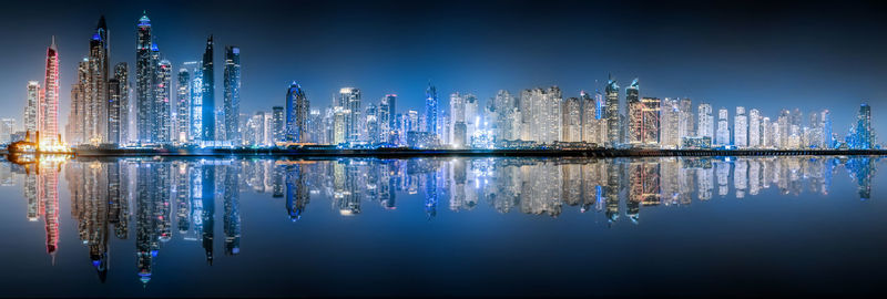 Panoramic view of illuminated buildings by sea against blue sky