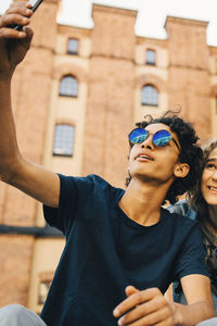 Fashionable teenage boy taking selfie with friend in city