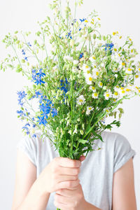 The woman holds the bouquet with both hands and covers her face. minimal composition with wild